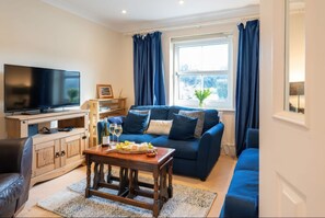 A living room with a TV, sofa, coffee table, and a window with curtains. - 17 Solent Landing, Bembridge (Bembridge)