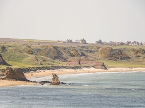 A coastal landscape with a beach, rocky outcrops, and distant buildings. - SEA BREEZE COTTAGE, enclosed courtyard, in Cullen (Buckie)