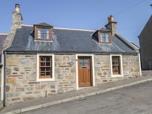 A stone building with a gabled roof, two windows, a door, and a chimney. - SEA BREEZE COTTAGE, enclosed courtyard, in Cullen (Buckie)