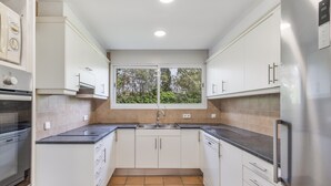 Una cocina moderna con armarios blancos, un refrigerador de acero inoxidable y una ventana con vista a árboles.
