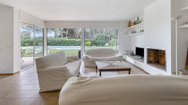 Una sala de estar moderna con un gran ventanal que da a un jardín, una chimenea y un televisor sobre un mueble.