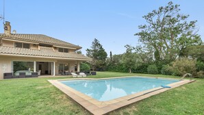 Una casa con piscina, un patio con mobiliario exterior y un jardín.