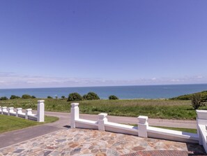 Eine Steinterrasse mit einem weißen Zaun und Blick auf das Meer.