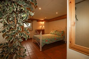 A bedroom with a bed, a bedside table, a lamp, and a large potted plant. - The Cave in Newquay, Cornwall. (Newquay)