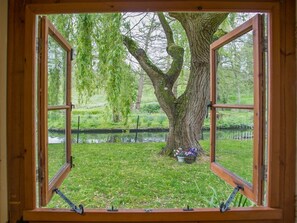 A window with a view of a tree, grass, and a small pond. - Weir Cottage, Hollingbourne (Maidstone)