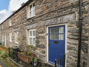 A stone building with a blue door, numbered 5, and a small garden area with plants. - Charming Noddfa in Penmachno (Betws-y-Coed)