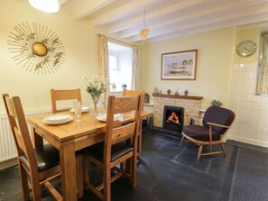 A dining area with a wooden table and chairs, a fireplace, a clock, and a sunburst wall decoration. - Charming Noddfa in Penmachno (Betws-y-Coed)
