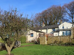 Una casa de dues plantes amb mur de pedra, un jardí petit i un arbre.