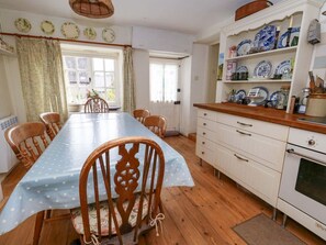 A kitchen with a wooden table, chairs, a white stove, and a shelf with blue and white dishes. - Little Orchard, Chard (Chard)