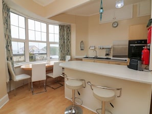 A kitchen with a dining area, bar stools, a refrigerator, and a view through large windows. - Capstone View Ilfracombe 2-bed (Ilfracombe)