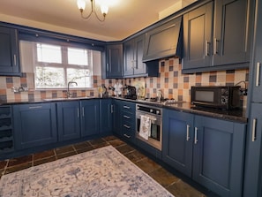 A kitchen with blue cabinets, a tiled backsplash, a stove, a microwave, and a window with blinds.