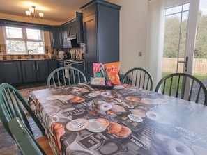 A kitchen with dark cabinets, a dining table with a coffee-themed tablecloth, and a bag of snacks on the table.