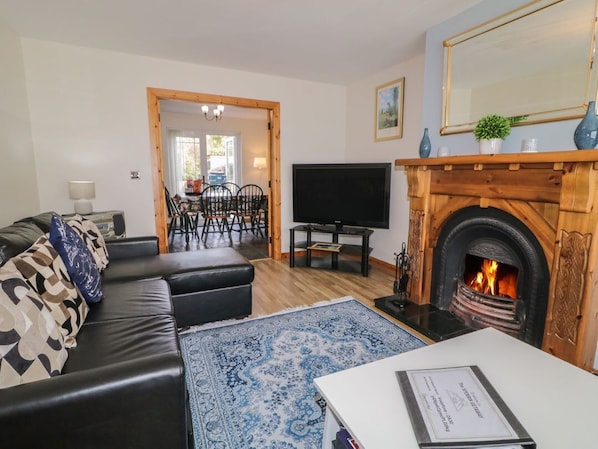 A living room with a fireplace, a sofa, a TV, and a dining area in the background.