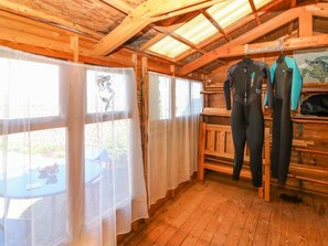 A wooden cabin interior with a high ceiling, wooden beams, a table with chairs, and a wetsuit rack. - Jade Cottage, Macduff, Banff. (Macduff)