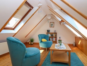 A cozy attic room with a sloped ceiling, a wooden table, two blue chairs, a bookshelf, and a small plant. - Jade Cottage, Macduff, Banff. (Macduff)