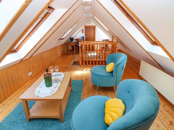 A cozy attic room with a wooden floor, a table with a bottle and glasses, two blue chairs, and a view of the room below. - Jade Cottage, Macduff, Banff. (Macduff)