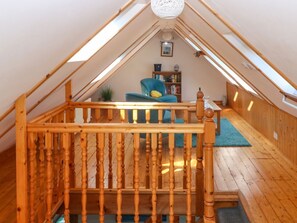 A loft bedroom with a wooden staircase, a blue chair, a bookshelf, and a small plant. - Jade Cottage, Macduff, Banff. (Macduff)