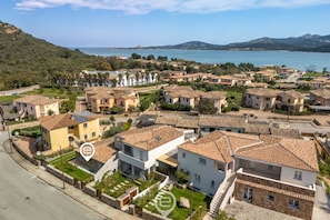 A residential area with houses, a road, and a body of water in the background. - Apt Ginevra 1 – Relax with terrace, garden and pool 🌿☀️ (Arzachena)