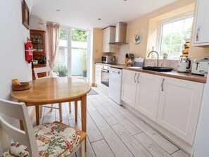 A kitchen with white cabinets, a wooden dining table, and a window. - The Stables is in Chester (Chester)