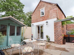 A brick house with a white exterior, a patio with metal chairs and a table, and a blue door. - The Stables is in Chester (Chester)