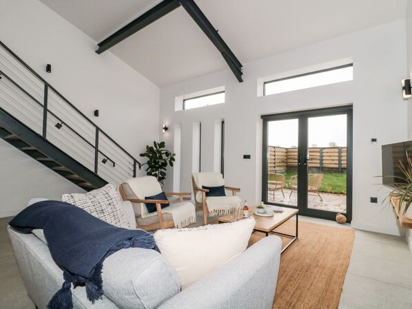 Una sala de estar moderna con un sofá, sillas, una mesa de centro, una escalera y un vidrio corredizo que da a un área exterior.