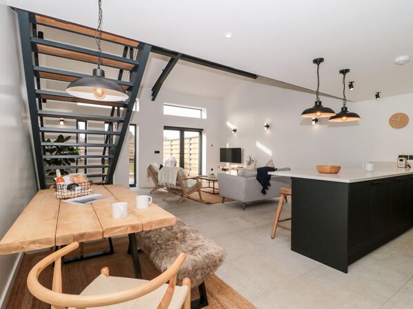 A modern kitchen with a central island, a dining area with a wooden table and chairs, and a staircase with a wooden railing.