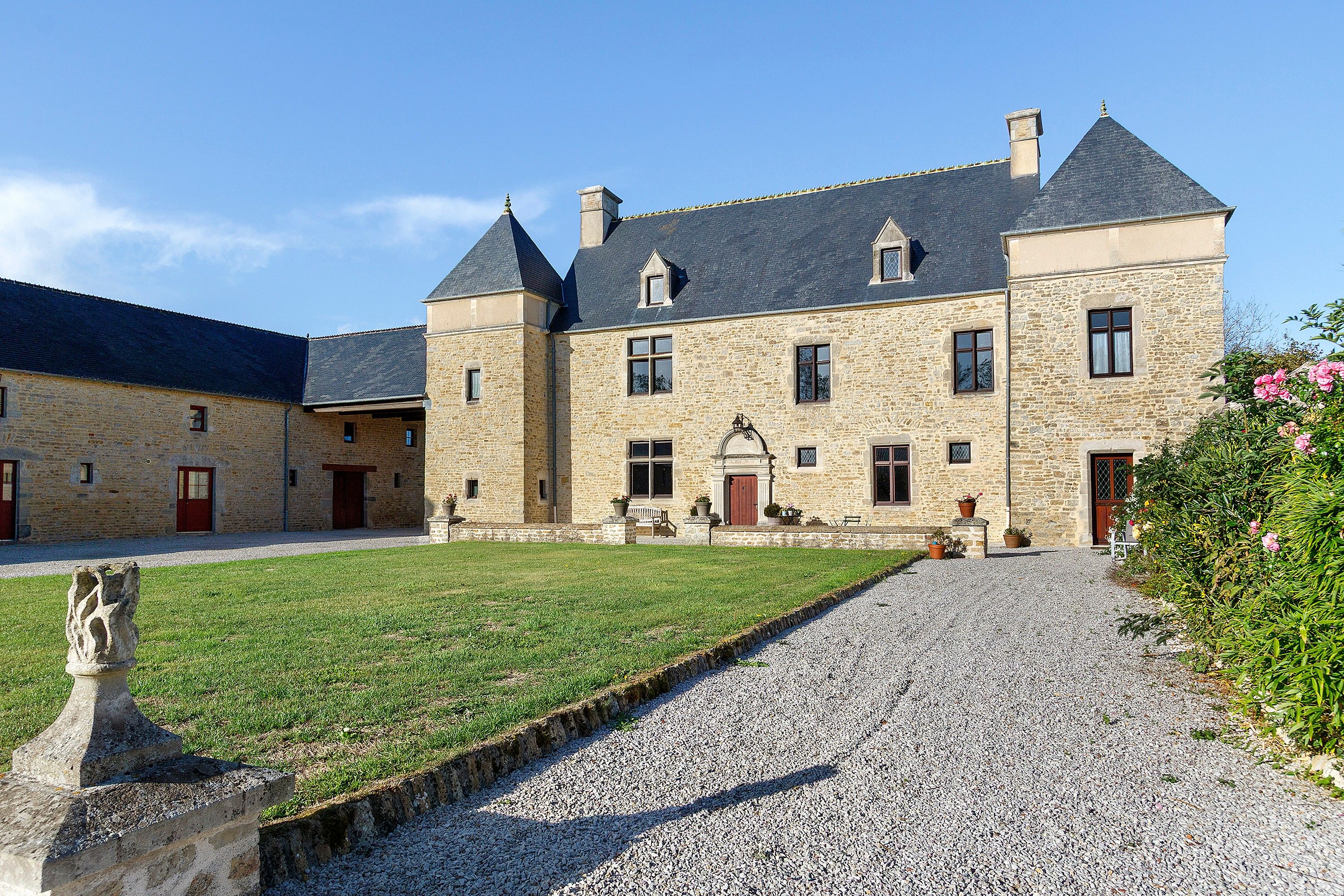Un bâtiment en pierre doté d’une cour, d’une allée gravillonnée et d’une statue.