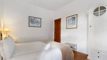 A bedroom with a bed, a bedside table, a lamp, a wardrobe, and two framed pictures on the wall.