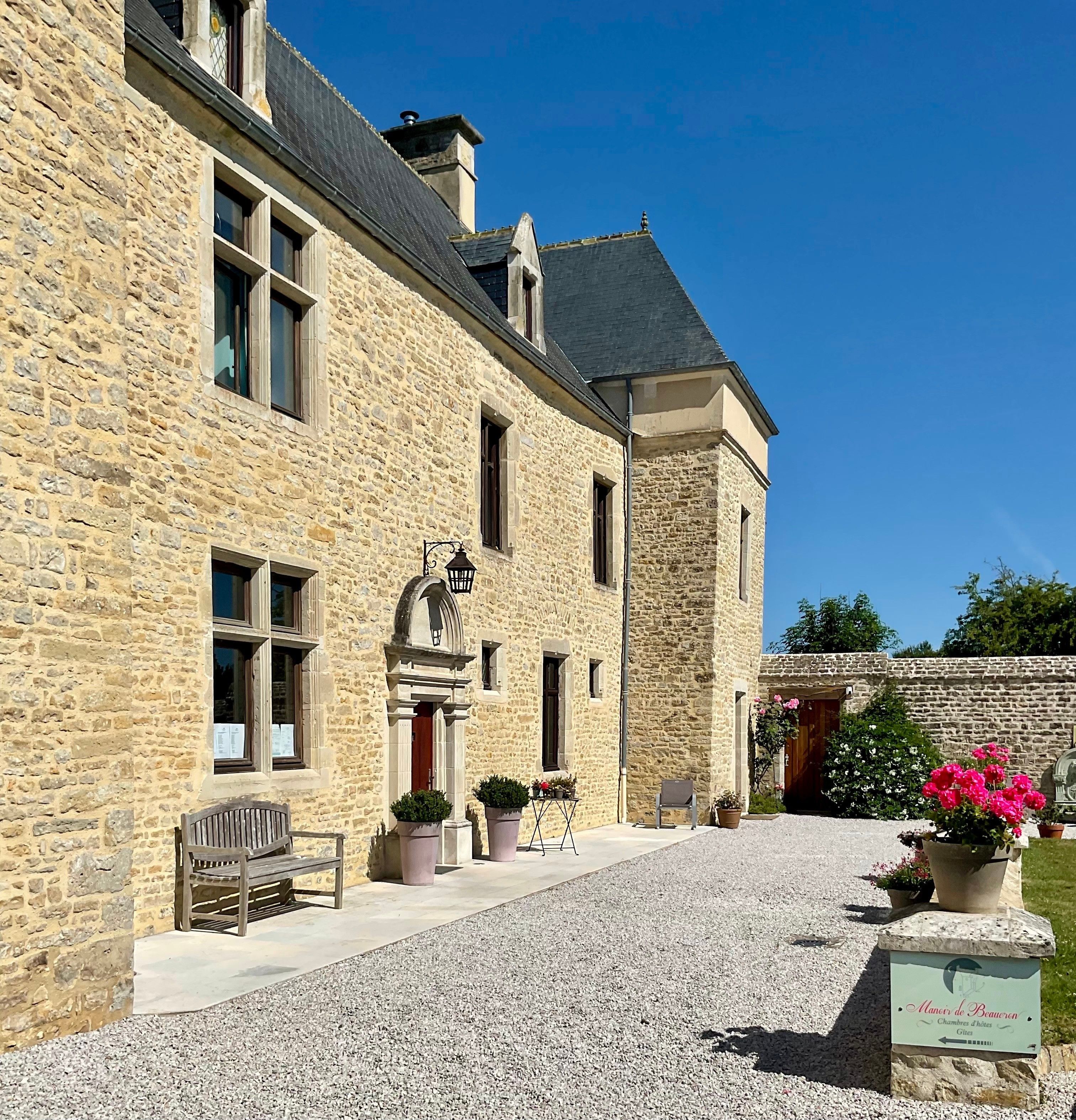 Un bâtiment en pierre avec une allée de gravier, un banc et des plantes en pot.