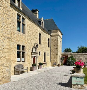 A stone building with a gravel driveway, a bench, and potted plants.