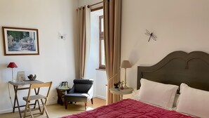 A bedroom with a bed, a desk, a chair, a small table, and a window with curtains.