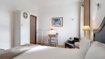 A hotel room with a bed, a desk, a chair, a lamp, and a framed painting on the wall.
