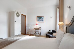 Ein Hotelzimmer mit einem Bett, einem Schreibtisch, einem Sessel, einer Lampe und einem gerahmten Gemälde an der Wand.