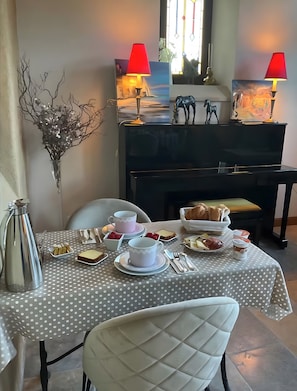 Un tavolo da pranzo con una tovaglia a pois, un vaso con dei rami, una caffettiera e un pianoforte sullo sfondo.