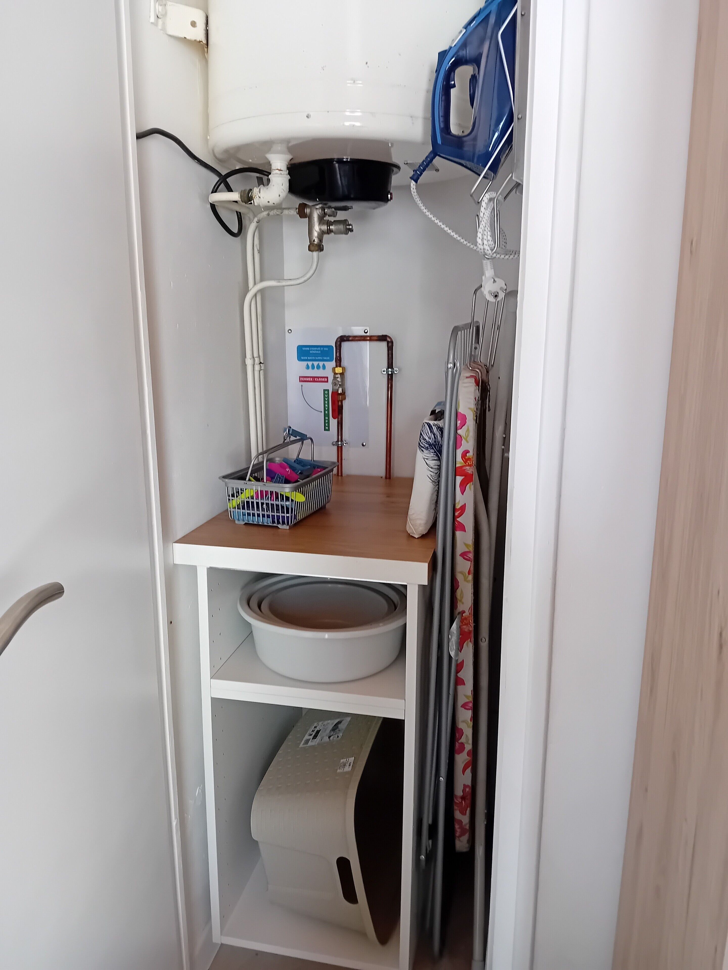 Un baño pequeño con inodoro, lavamanos, ducha y un estante de almacenamiento.