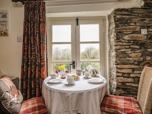 A cozy room with a stone wall, a round table set for tea, and a window with curtains. - The Mill, Lostwithiel (Lostwithiel)