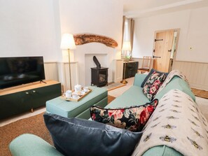 A living room with a television, a fireplace, a sofa, and a wooden beam on the wall. - Natland Hall Cottage in Kendal (Kendal)