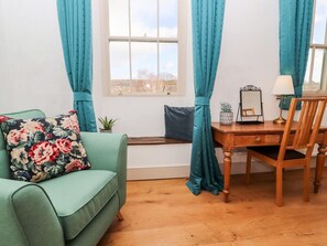 A room with a green sofa, a wooden desk, a chair, a small table with a lamp, and a window with curtains. - Natland Hall Cottage in Kendal (Kendal)