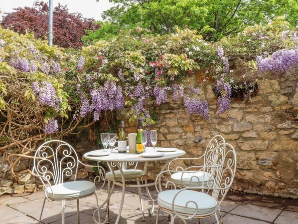 A stone wall with purple flowering vines, a round table with chairs, and bottles of wine. - Old Rectory Cottage, Washingborough (Lincoln)