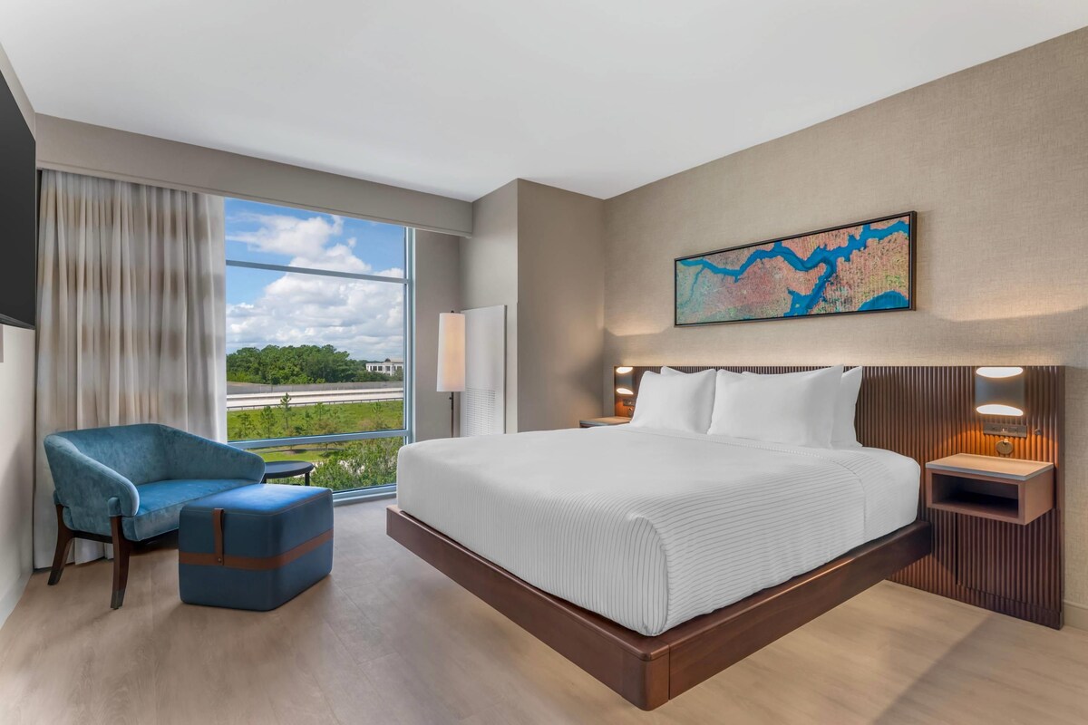 Una habitación de hotel con una cama grande, un sillón azul, una mesita de noche, una lámpara y un mapa en la pared.