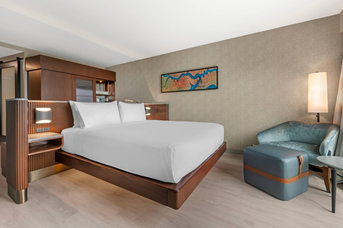 Quarto de hotel com uma cama grande, área de estar e uma obra de arte pendurada na parede.