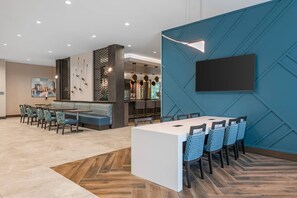 Ein moderner Essbereich mit einem langen Tisch und Stühlen, eine Bar mit Sitzgelegenheiten und ein großer Fernseher an einer blauen Wand.