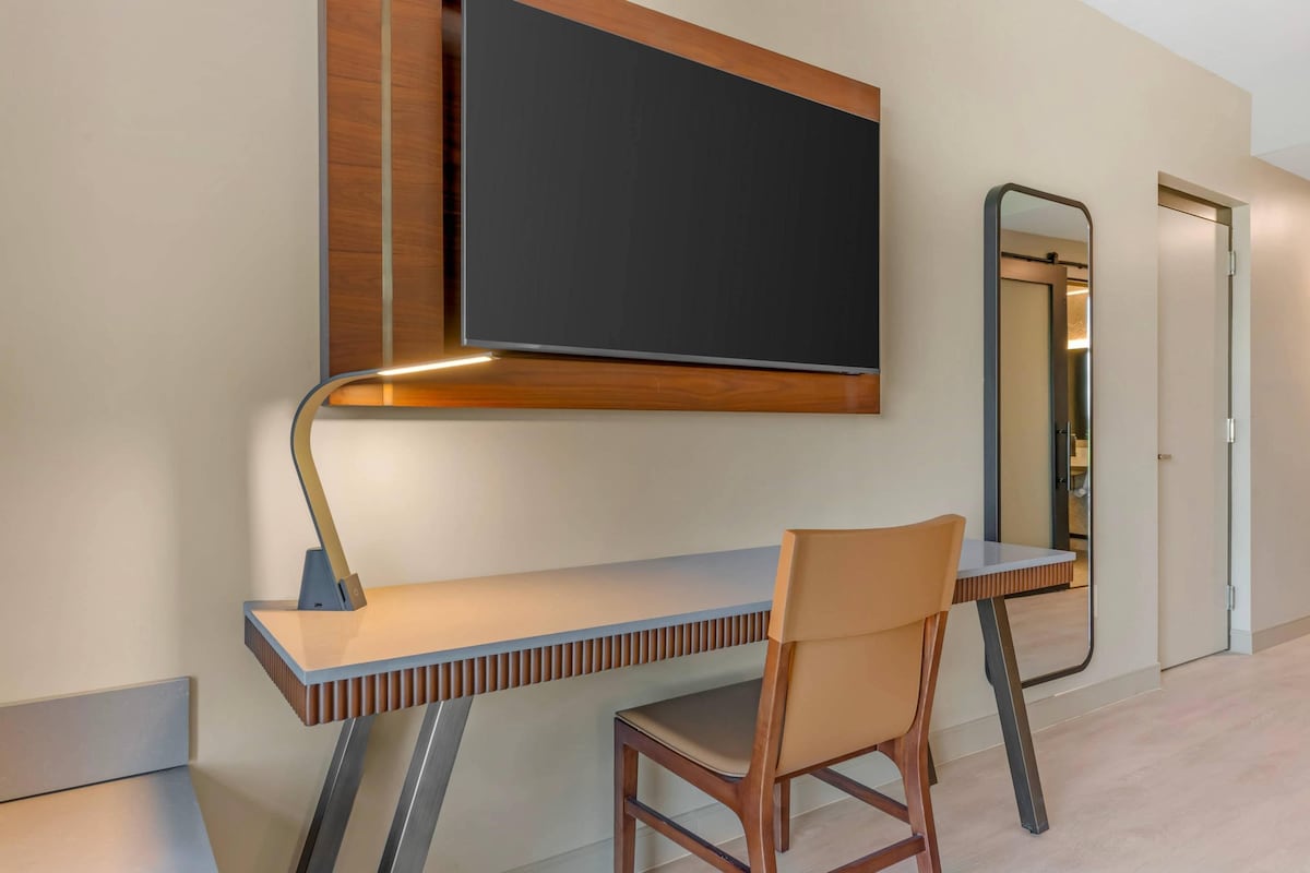 A modern workspace with a flat-screen TV mounted on the wall, a wooden desk, a chair, and a mirror.