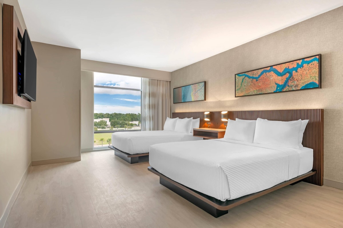 Ein Hotelzimmer mit zwei Betten, einem großen Fenster mit Blick und zwei Wandbildern.