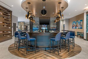 Eine Bar mit einer gebogenen Theke, mehreren Barhocker und Pendelleuchten an der Decke.