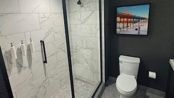 A modern bathroom with a glass-enclosed shower, a toilet, and a framed picture on the wall.