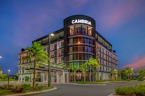 Ein mehrstöckiges Hotel mit einem gut sichtbaren 'CAMBRIA'-Schild, das ein modernes architektonisches Design mit Glas- und Metallelementen aufweist.