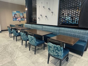 A restaurant interior with a long counter, blue upholstered seating, and a cityscape painting. - Cambria Hotel Jacksonville (Jacksonville)