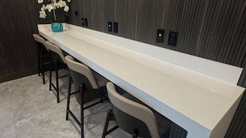 Una cocina alargada y estrecha con encimera blanca, cuatro taburetes de bar y un florero con flores blancas a la izquierda.