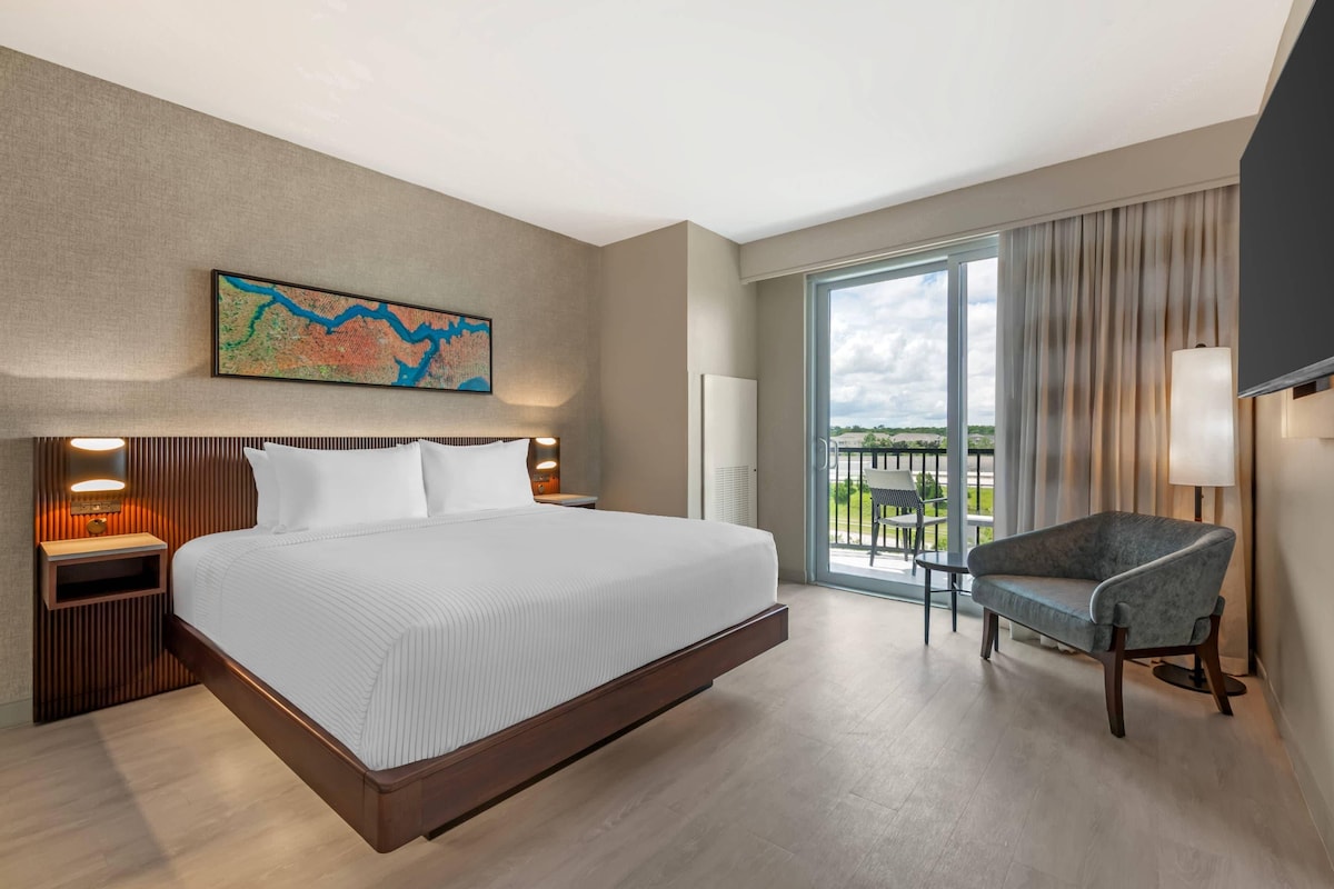 Ein Hotelzimmer mit einem großen Bett, einem Sessel, einer Karte an der Wand und einem Balkon mit Blick.